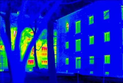 A thermal camera shows heat escaping: the building on the left glows (heat leaking out), the insulated one on the right stays cool.